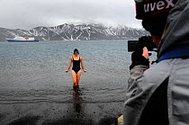 A tourist coming out of the water after a swim in hot springs, Deception Island, with Antarctic cruise liner 'MV Ushuaia' in the background. Antarctica.
