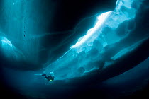 Scuba diver under and between ice formations, Lake Sassolo, Sambuco valley, Ticino, Switzerland. Model released.