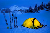 Yellow tent illuminated in the waning twilight hours on the shores of frozen Garibaldi Lake with a view of Mount Price in the background. Garibaldi Provincial Park. Britisth Columbia, Canada, March 20...