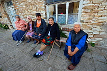 Women sitting on bench in village, Eastern Rhodope Mountains, Plevun, Bulgaria, May 2013.