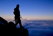 Climber silhouetted on Mount Rainier with Mount Adams in the distance, Mount Rainier National Park, Washington, USA. Model Released.