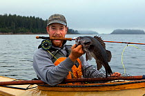 Man with Black rockfish (Sebastes melanops) caught with a fly rod in the Strait of Juan de Fuca. Washington, USA. July 2013. Model released.