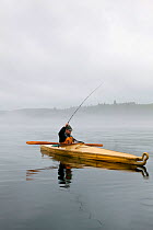 Man in kayak fishing with his home made bamboo fly rod on a foggy morning in the Strait of Juan de Fuca, Washington, USA, August 2013.