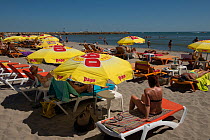 People on sun loungers on the beach during summer, Saintes Maries de la mer. Camargue, France. June 2013.
