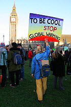 Environmental protester infront of houses of parliment holding up placard stating 'To be cool stop global warming' London UK