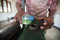 Man pouring Jatropha biofuel from a bottle to fuel a milling machine, Tanzania.