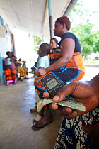 Tanzanian women holding mobile phone and cash, waiting to power up at a solar-powered charging booth, Miono Region, Tanzania.