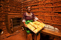 Tanzanian woman with freshly baked bread loaves and energy efficient coal oven, Miono Region, Tanzania