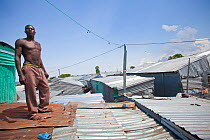 Man standing on corrugated roof in shanty town, Remba Island, Lake Victoria, Kenya.
