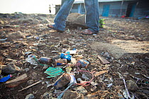 Man walks past discarded batteries littering the ground on Remba Island, Lake Victoria, Kenya