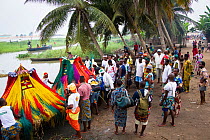 Men watching 'Zangbeto', traditional voodoo guardians of the night in the Yoruba religion, are helped in to boat to journey to another village for Voodoo / Vodun ceremony, Benin, February 2011.