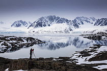 Landscape photographer taking a picture of the view across the Liefdefjorden, towards the Monacobreen Glacier, Spitzbergen, Svalbard, Norway, June, 2012. Model released.
