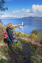Woman walker enjoying the view to Rubha Nan Gall Lighthouse, North of Tobermory, Isle of Mull, Scotland, UK, May 2013.