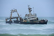 Wrecked boat aground in storm, with Cape cormorant (Phalacrocorax capensis) colony, near the coast of the Skeleton Coast National Park, Namibia, September 2013.