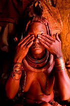 Himba woman applying Otjize (a mixture of butter, ochre and ash) to her skin, Kaokoland, Namibia, September 2013.