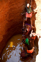 Children drinking water in a deep well dug into the dry bed of a river. Kaokoland, Namibia.