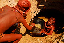 Himba women drawing water from a well dug into the dry riverbed well, Kaokoland, Namibia, February 2005.
