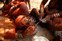 Himba women braiding hair each other's hair, Kaokoland, Namibia, September 2013.