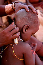 Himba mother shaving sons hair, Kaokoland, Namibia, September 2013.