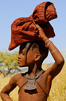 Himba girl carrying bag on her head, Kaokoland, Namibia, June 2006.