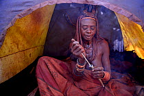 Himba woman snorting nasal snuff tobacco in camping tent, Himba village, Kaokoland, Namibia, September 2013.