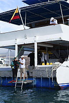 Dive master helping guest diver check equipment. Galapagos Aggressor live-aboard dive boat, Galapagos Islands. September 2011. Property and model released.