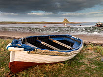 Fishing boat on shore with Lindisfarne Castle in the distance, Holy Island, Northumberland, UK, April 2013.