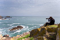 Photographer taking pictures of coastal landscape with rocky headland. Great Saltee, Saltee Islands, County Wexford, Republic of Ireland, June.