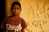 Boy standing by animal relief sculptures on mud of house wall, in indigenous Tharu village, Terai, Bardia National Park, October 2011.
