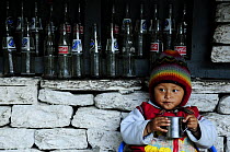 A child drinking by wall with empty glass bottles, in the small village of Khumnu. Annapurna Sanctuary, central Nepal, November 2011.