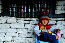 A child sitting by wall with empty glass bottles, in the small village of Khumnu. Annapurna Sanctuary, central Nepal, November 2011.
