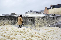 Person walking through sea foam as waves crash into Saint-Guenole during Storm 'Petra', Finistere, Brittany, France. 5th February 2014.  France, Bretagne, Finistere, Saint-Guenole, Tempete "Petra",...