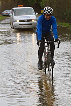 Cyclist in waterproof clothing cycling through flood water during the February 2014 flooding, Upton upon Severn, Worcestershire, England, UK, 9th February 2014.