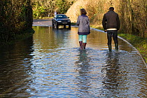 Couple walking in flooded road with stranded car during January 2014 floods, Somerset Levels, England, UK, 11th January 2014.