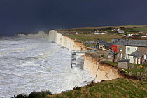 Waves crashing against chalk cliffs, with houses close to edge of cliffs, during a winter storm at Birling Gap, Sussex, England, UK, 15th February 2014.