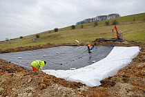 Medieval dewpond, originally lined with clay being re-lined with plastic sheeting as part of the Marlborough Downs Nature Improvement Area project, Barbury Castle, Wiltshire, UK, March 2013.