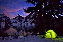 Tent lit up at night after an early winter snowfall, with Kaleetan Peak and Gem Lake, near Snoqualmie Pass, Cascades,  in Washington, USA, October 2013.