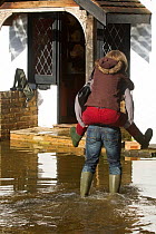 Resident giving a piggy back ride outside flooded home during February 2014 flood. Surrey, England, UK, 16th February 2014.