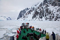 Tourists lining the deck ship Ushuaia in the Lemaire Channel clogged with sea ice, Antarctica.