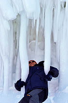 Man standing underneath cliff of large icicles, Lake Baikal, Siberia, Russia, March.