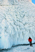 Ice formation caused by splashing water, with man standing underneath for scale, Lake Baikal, Siberia, Russia, March.