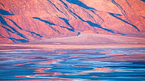 Early morning over distant mountains, creating vibrant reflections in the salt flats of Death Valley National Park, California, USA, December 2013.