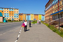 Pedestrians walking in the street among brightly coloured apartment blocks in Anadyr, Chukotka, Eastern Siberia, Russia. July 2013.