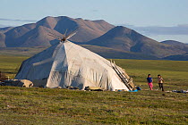 Chukchi children playing outside a Yaranga (traditional tent) at a reindeer herders' summer camp on the tundra with mountains of the Chukotsky Range in the backgrounds. Iultinsky District, Chukotka, S...
