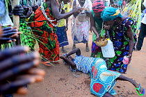 Woman lying on floor being sprinkled with water during Nalu ritual ceremony, Cabedu village, Guinea-Bissau, December 2013.
