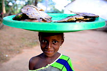 Young fish seller carrying tray on head, Iemberem village. Cantanhez National Park, Guinea-Bissau, December 2013.