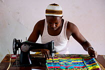Man sewing colourful loom woven fabric at Artisan Centre, Guinea-Bissau, December 2013.