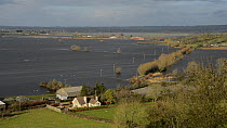 Overview of farm buildings at the edge of extensively flooded pasture land, with flooded farm tracks and road, West Sedgemoor, Somerset Levels, England, UK, February 2014.