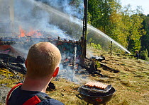 Firemen extinguishing controlled fire in abandoned house during training exercise whilst another rests and cooks sausages on a barbeque, Akerhus, Norway, September 2013.