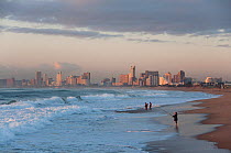 People on Durban beach at dawn with city in the distance, Durban, KwaZulu-Natal, South Africa, August 2009.